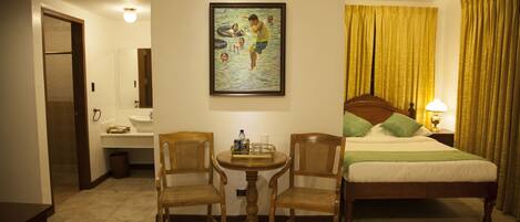 Habitación de hotel con cama, dos sillas, una mesita, un cuadro, un lavamanos y un espejo.