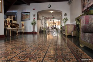 Un vestíbulo con suelo estampado, un mostrador de recepción y muebles clásicos, incluyendo un sofá y sillones.