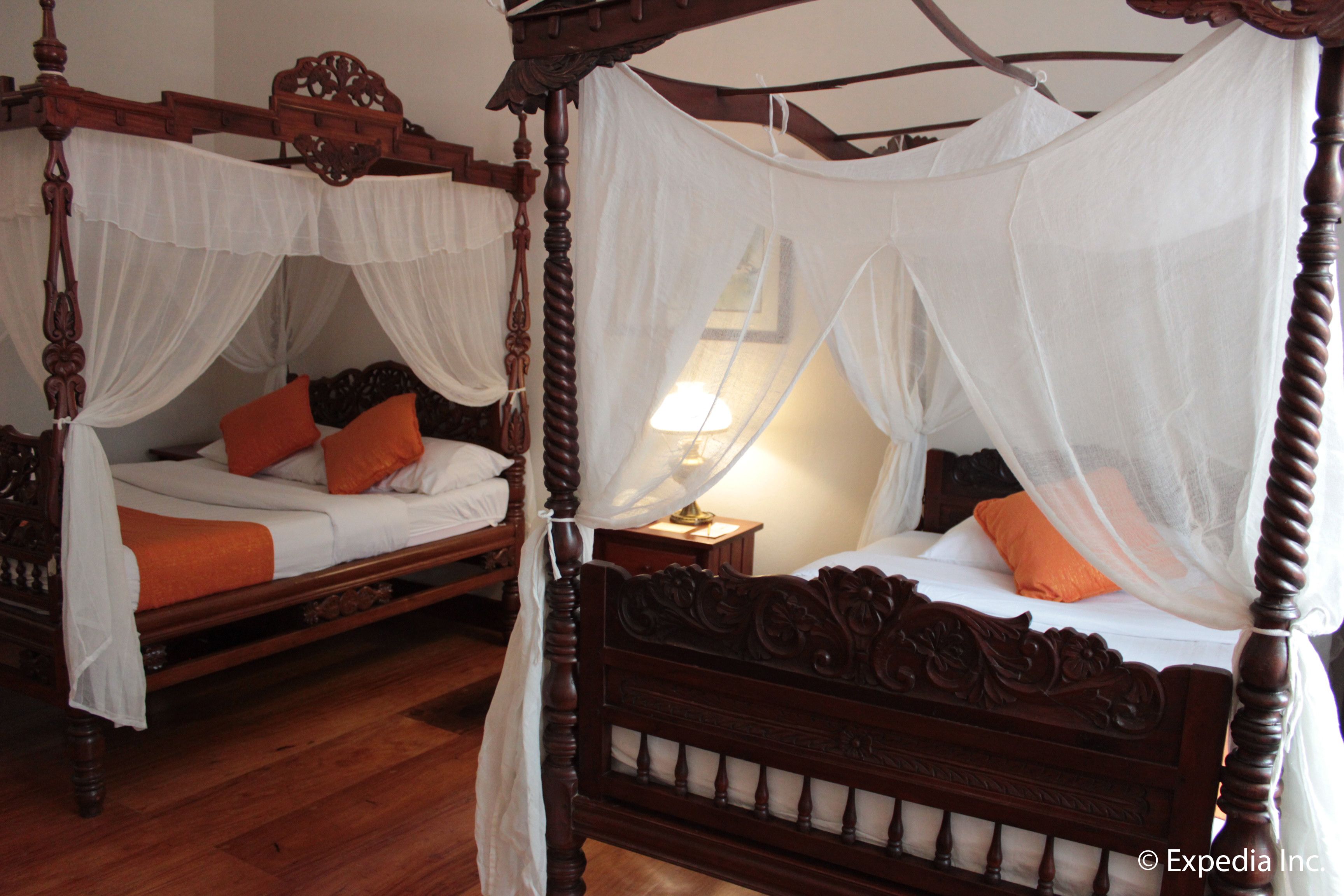 Un lit à baldaquin avec des rideaux blancs et des oreillers orange.