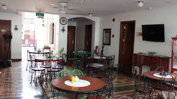 A dining area with multiple tables and chairs, a clock on the wall, and a television mounted on the wall.