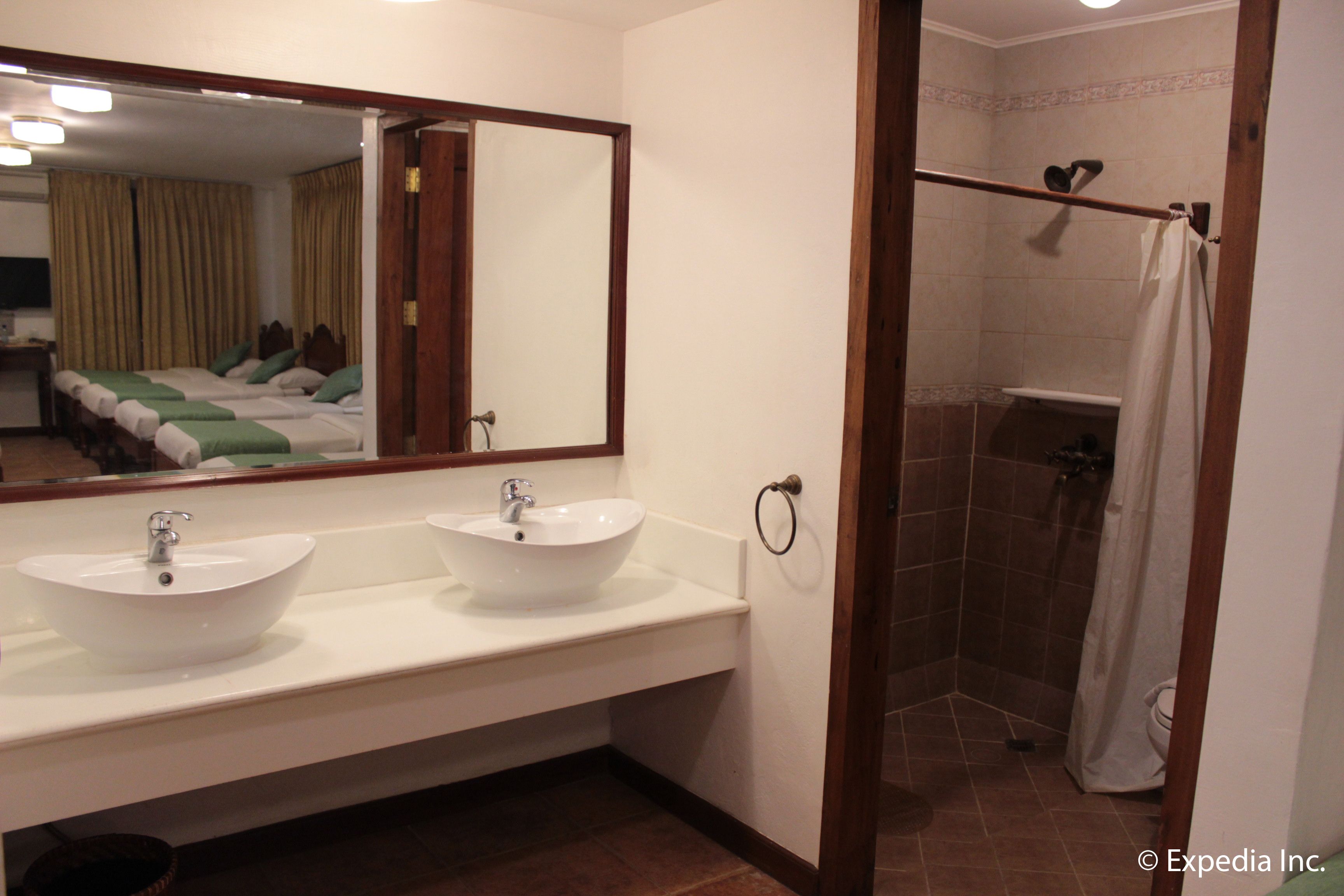 Un baño con dos lavamanos, un espejo, ducha y una puerta que da a un dormitorio.