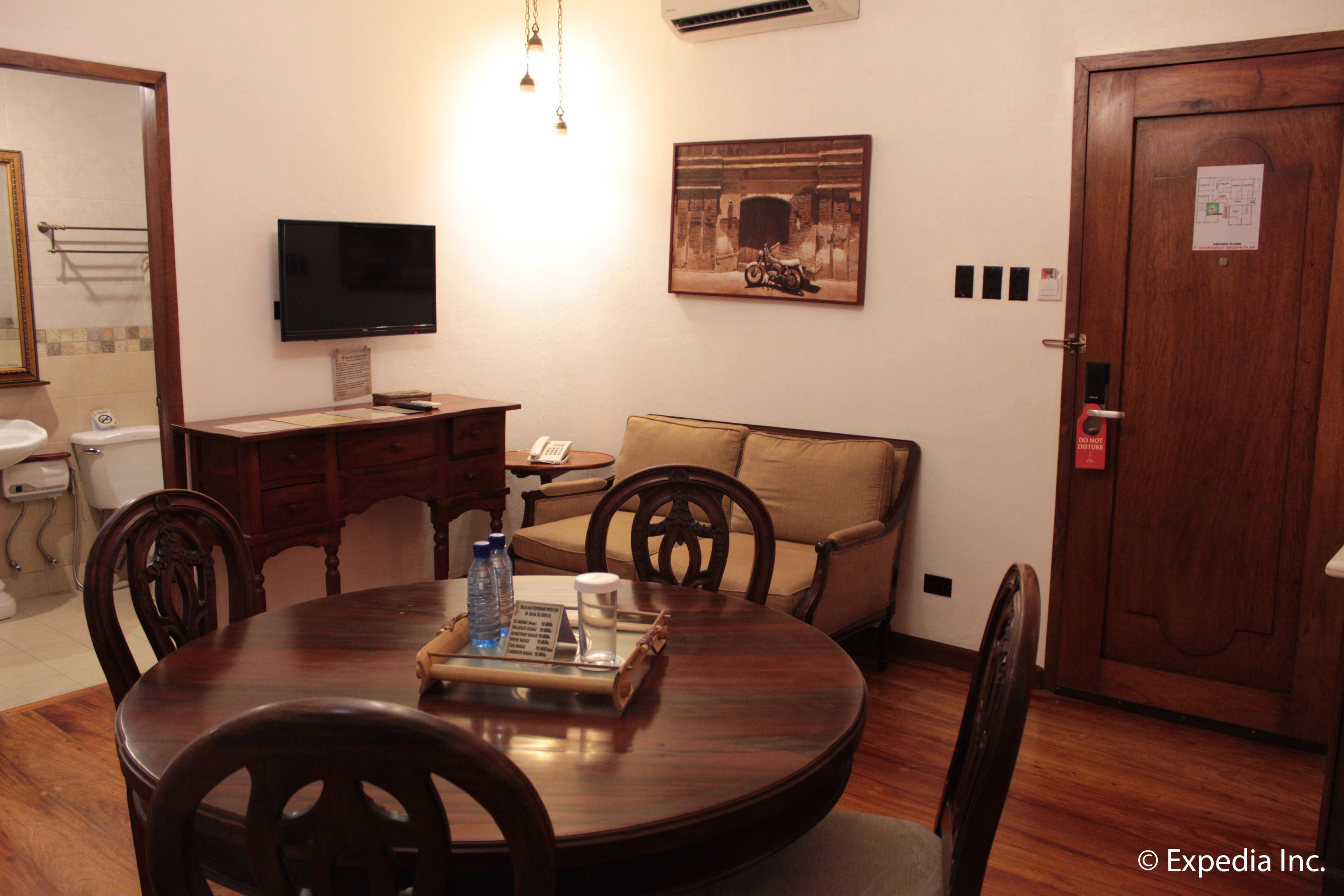 Un área de comedor con una mesa redonda de madera, sillas, un televisor montado en la pared, un sofá y una puerta con cerradura.