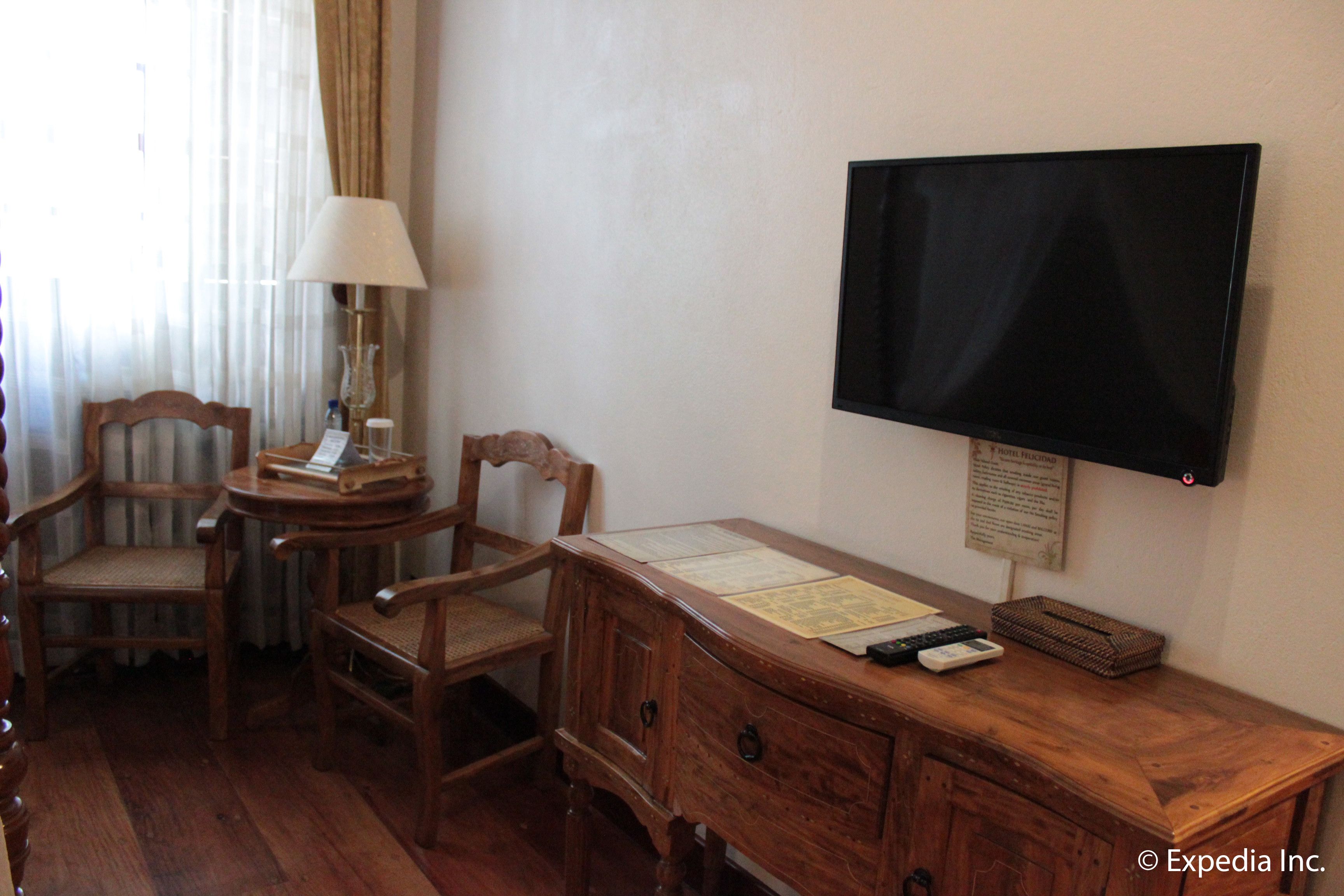 A hotel room with a wooden desk, two chairs, a television, and a lamp.