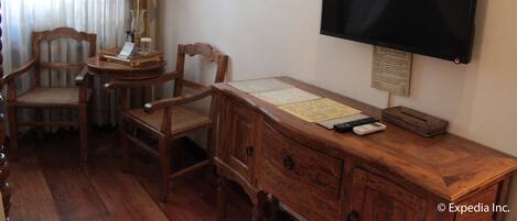 A hotel room with a wooden desk, two chairs, a television, and a lamp.
