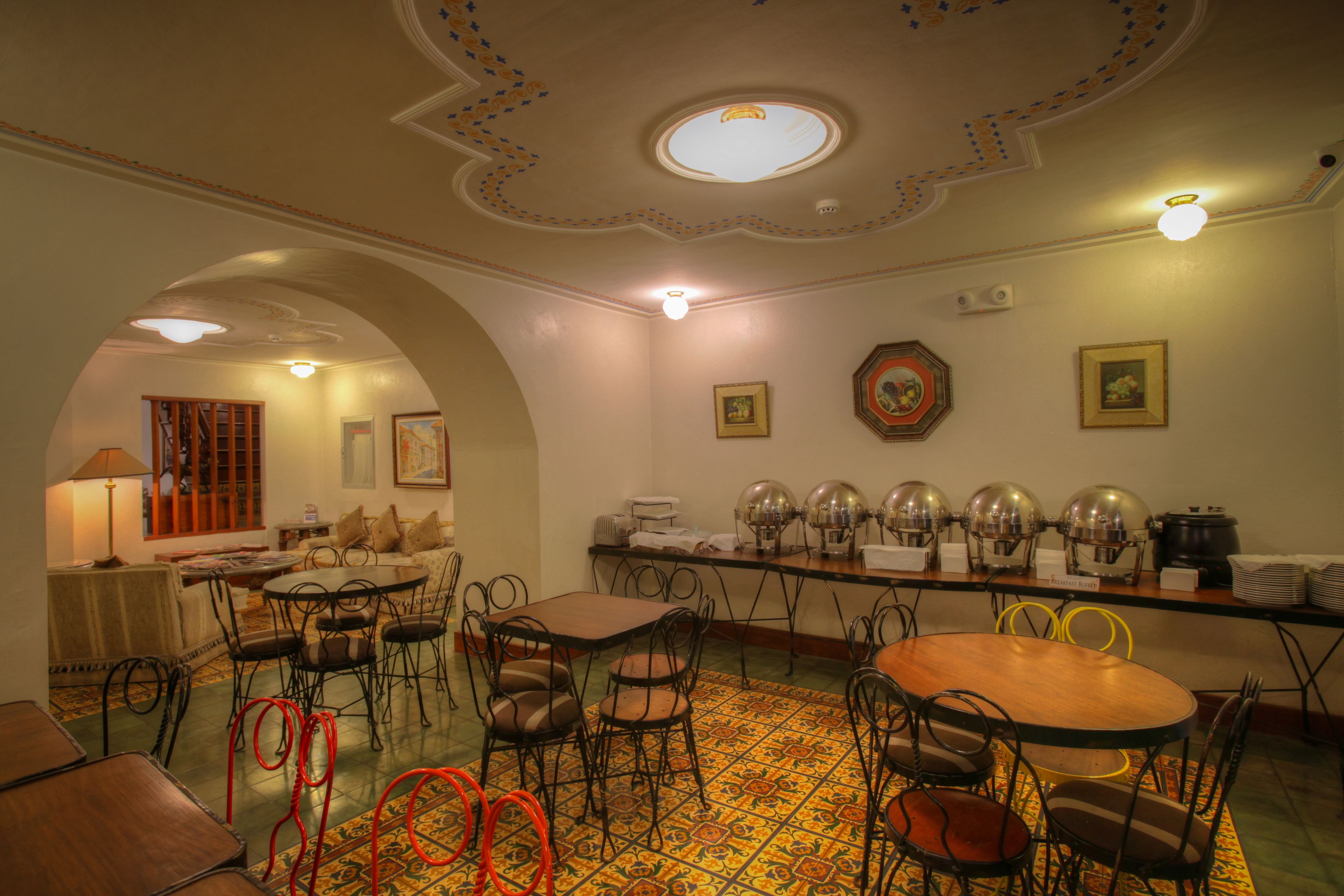 A dining area with round tables and chairs, a buffet setup, and a decorative ceiling.