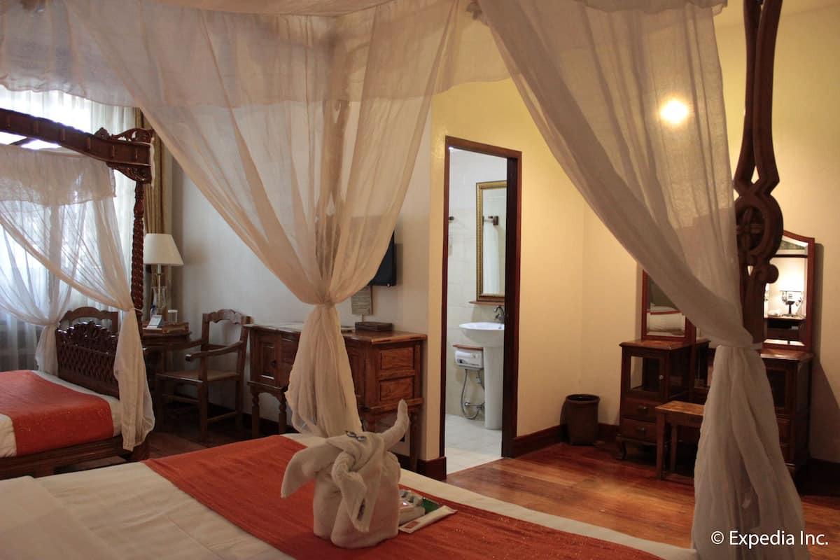 A bedroom with a canopy bed, a desk, and a bathroom visible through an open door.