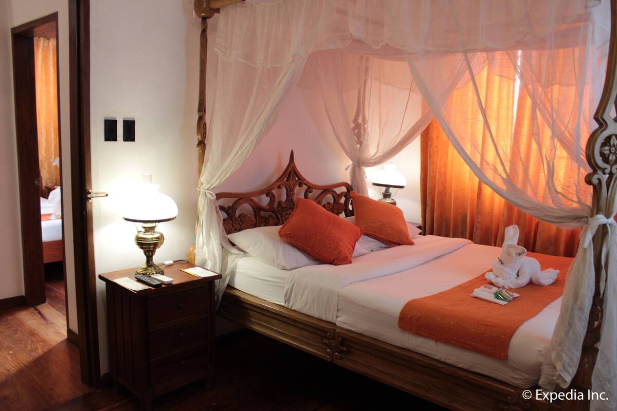 A four-poster bed with a canopy, a bedside table with a lamp, and a plush toy on the bed.