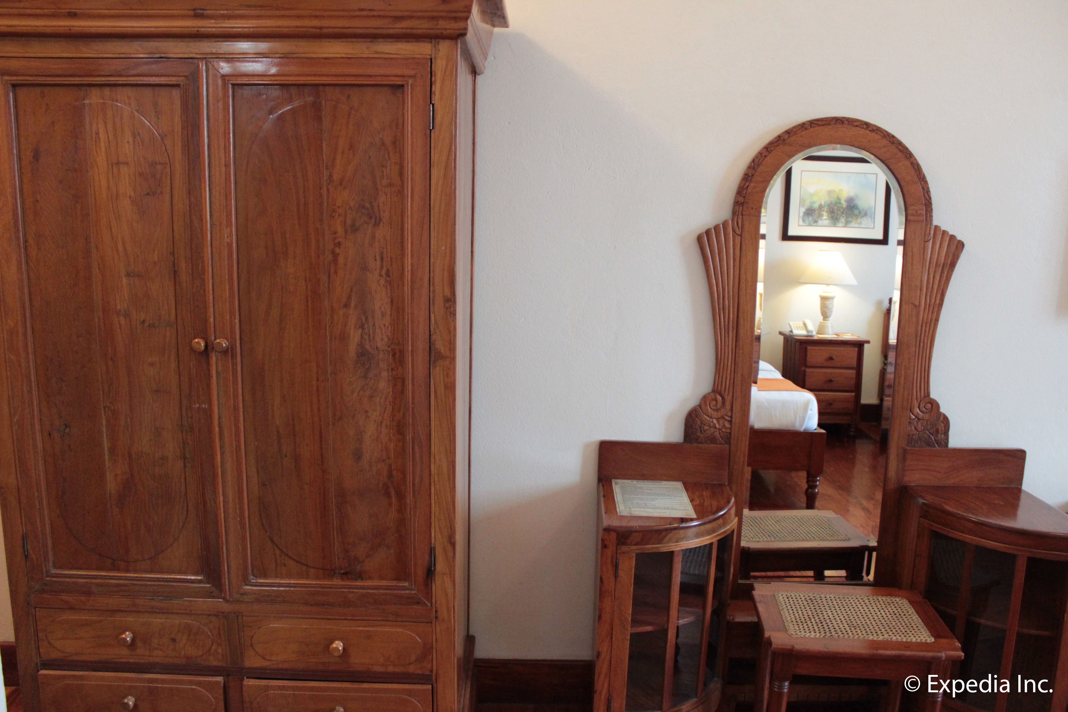A wooden wardrobe, a mirror, and a small table with chairs in a room.