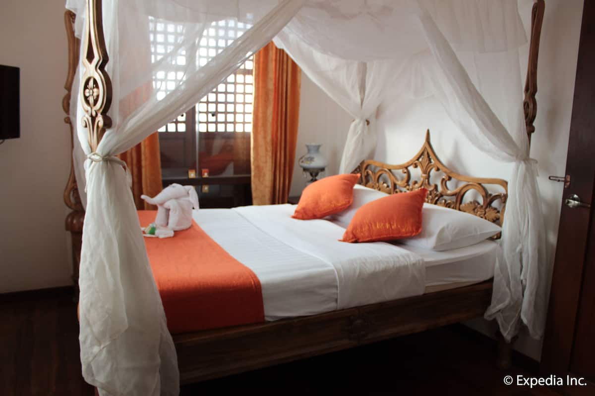 A four-poster bed with a canopy, white linens, and two orange pillows.