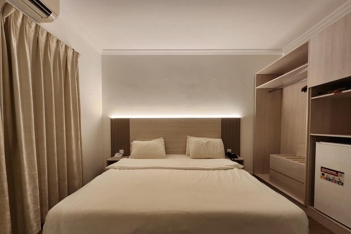 Una habitación de hotel con una cama grande, mesitas de noche, un armario y un equipo de aire acondicionado.
