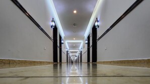 Un largo pasillo bien iluminado con piso reflectante, bordeado por paredes con cuadros enmarcados y puertas de marco negro.