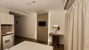 A hotel room with a bed, a desk with a mirror, a television, and an air conditioning unit.