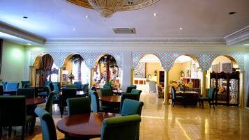 A spacious dining area with multiple tables and chairs, ornate ceiling design, and patterned walls.
