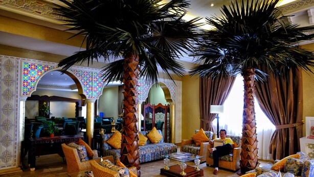 Un amplio salón con asientos cómodos, una palmera grande y una pared decorativa.