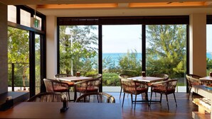Un comedor moderno con ventanas amplias, sillas de mimbre y vista al mar.