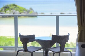 Habitación con vista a la playa y al océano, que incluye dos sillas de mimbre y una mesita redonda.