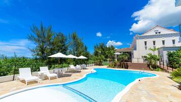 A swimming pool with lounge chairs and umbrellas, surrounded by a stone deck and lush greenery.