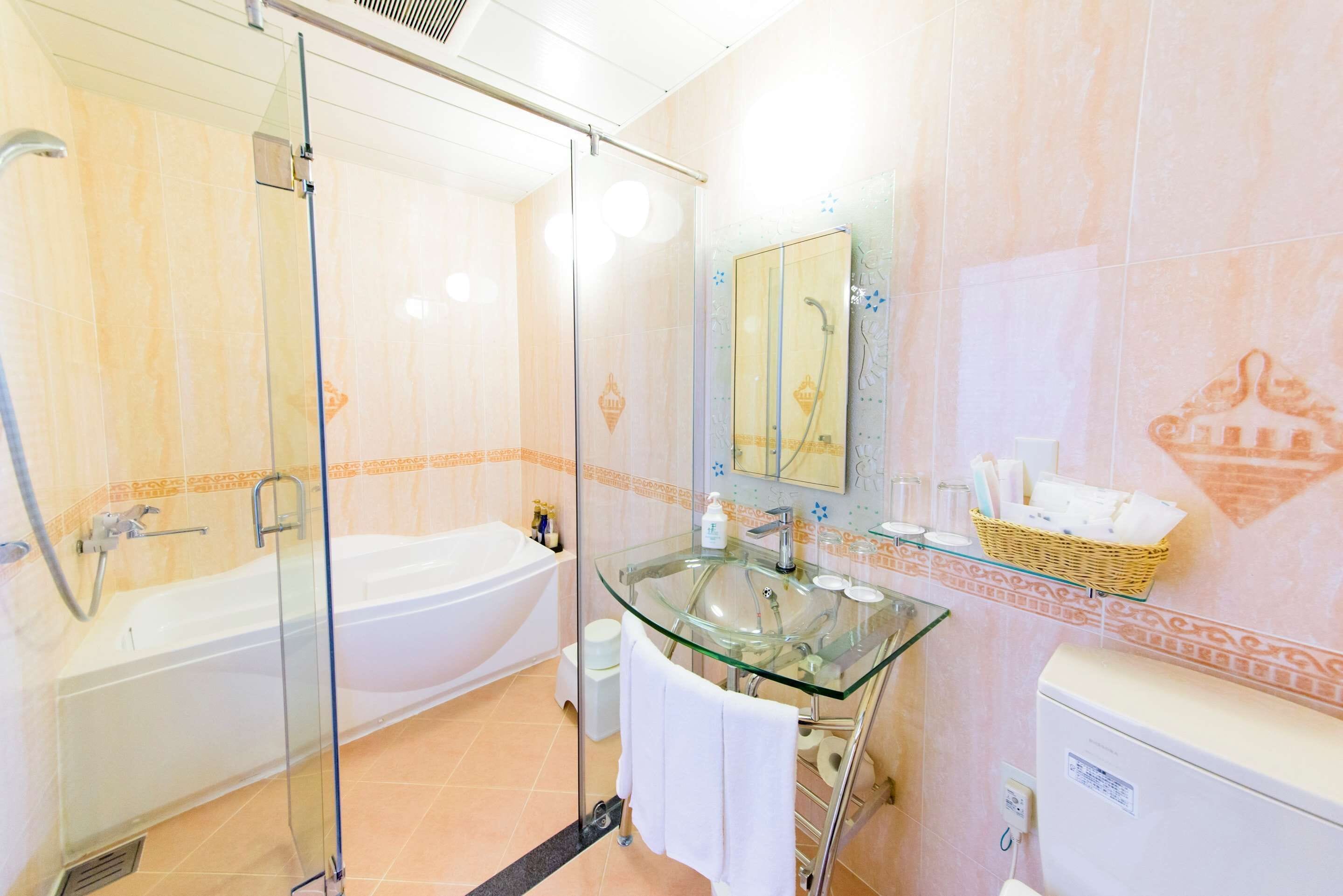 A bathroom with a glass-enclosed shower, a glass sink, a white bathtub, and a toilet.