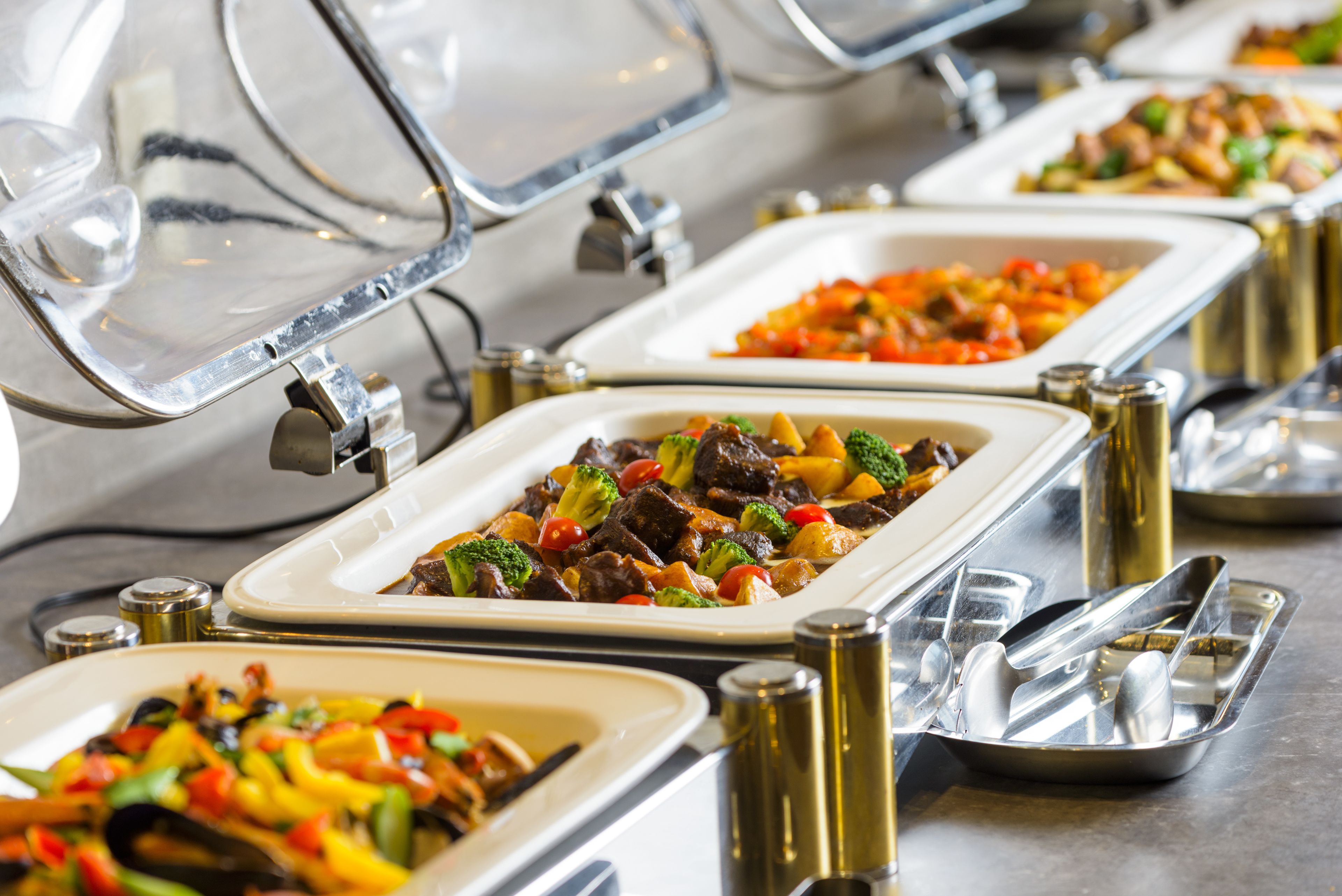 Speisen werden buffetförmig mit verschiedenen Gerichten, darunter Gemüse und Fleisch, in rechteckigen Schalen angeboten.