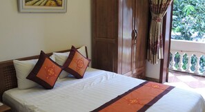 A hotel room with a bed, a wooden wardrobe, and a balcony with a view of greenery.