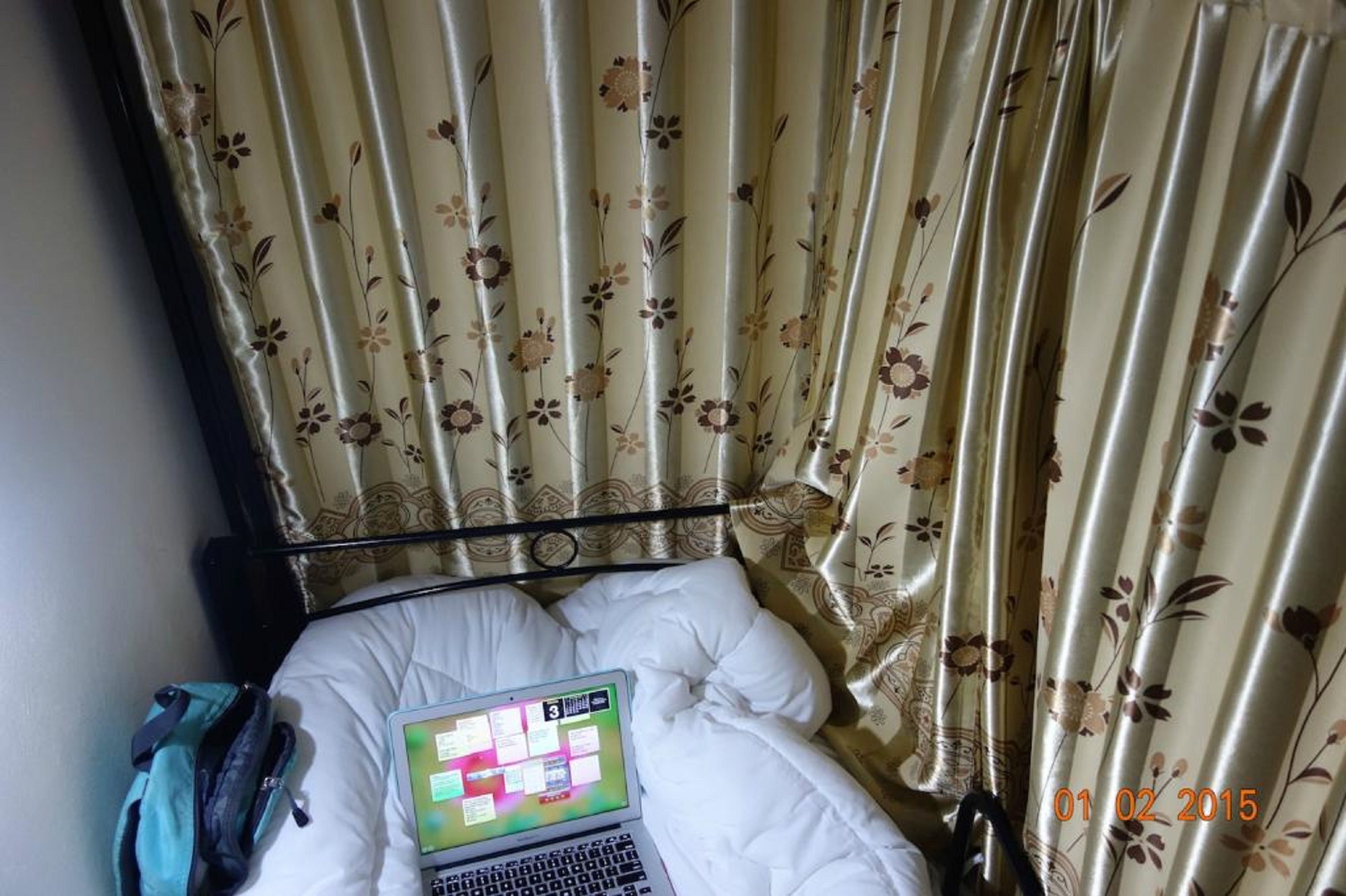 Ein Bett mit Laptop, Rucksack und Vorhängen mit Blumenmuster.