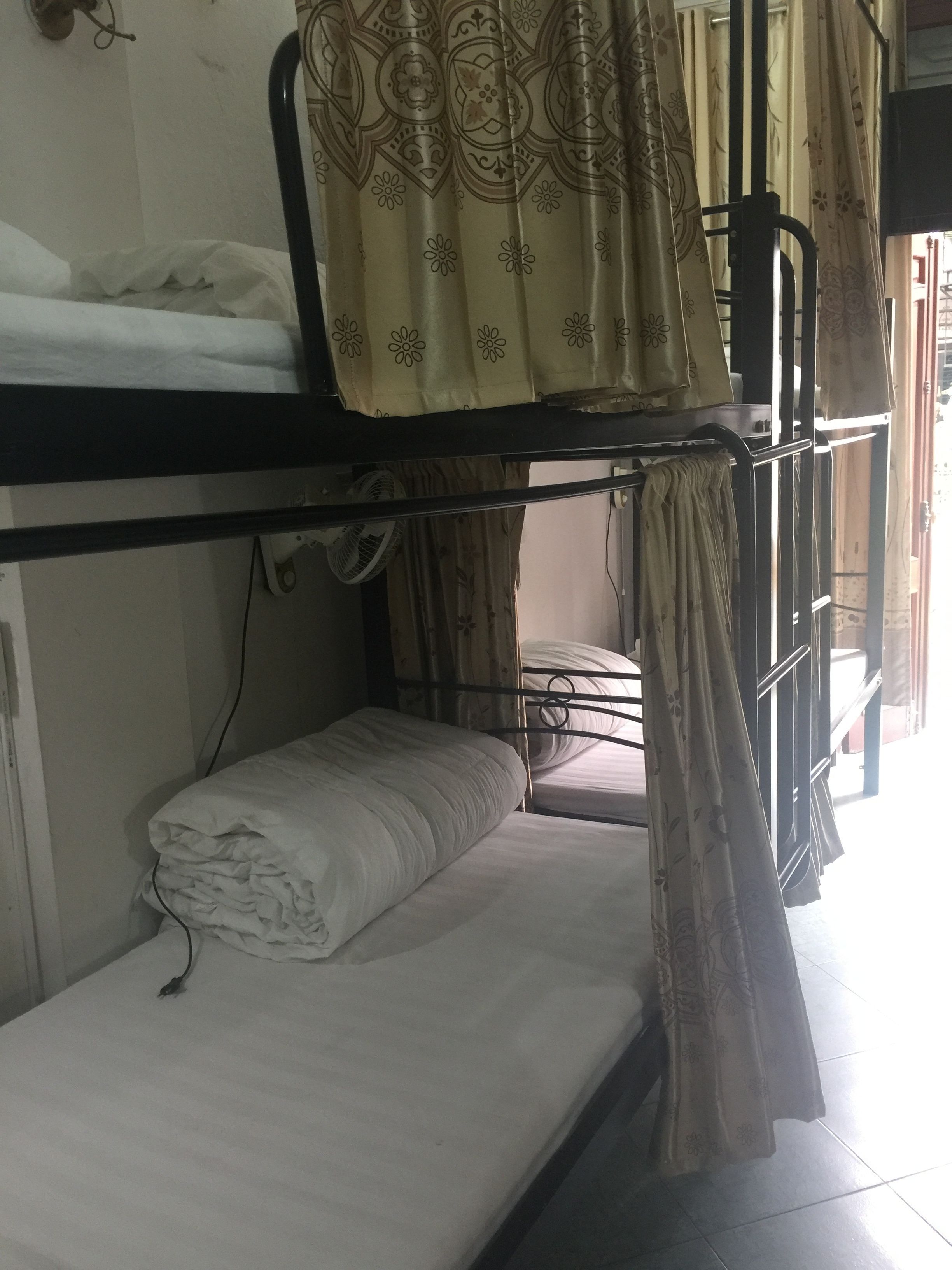 A bunk bed with a patterned curtain, a fan, and a power outlet on the wall.