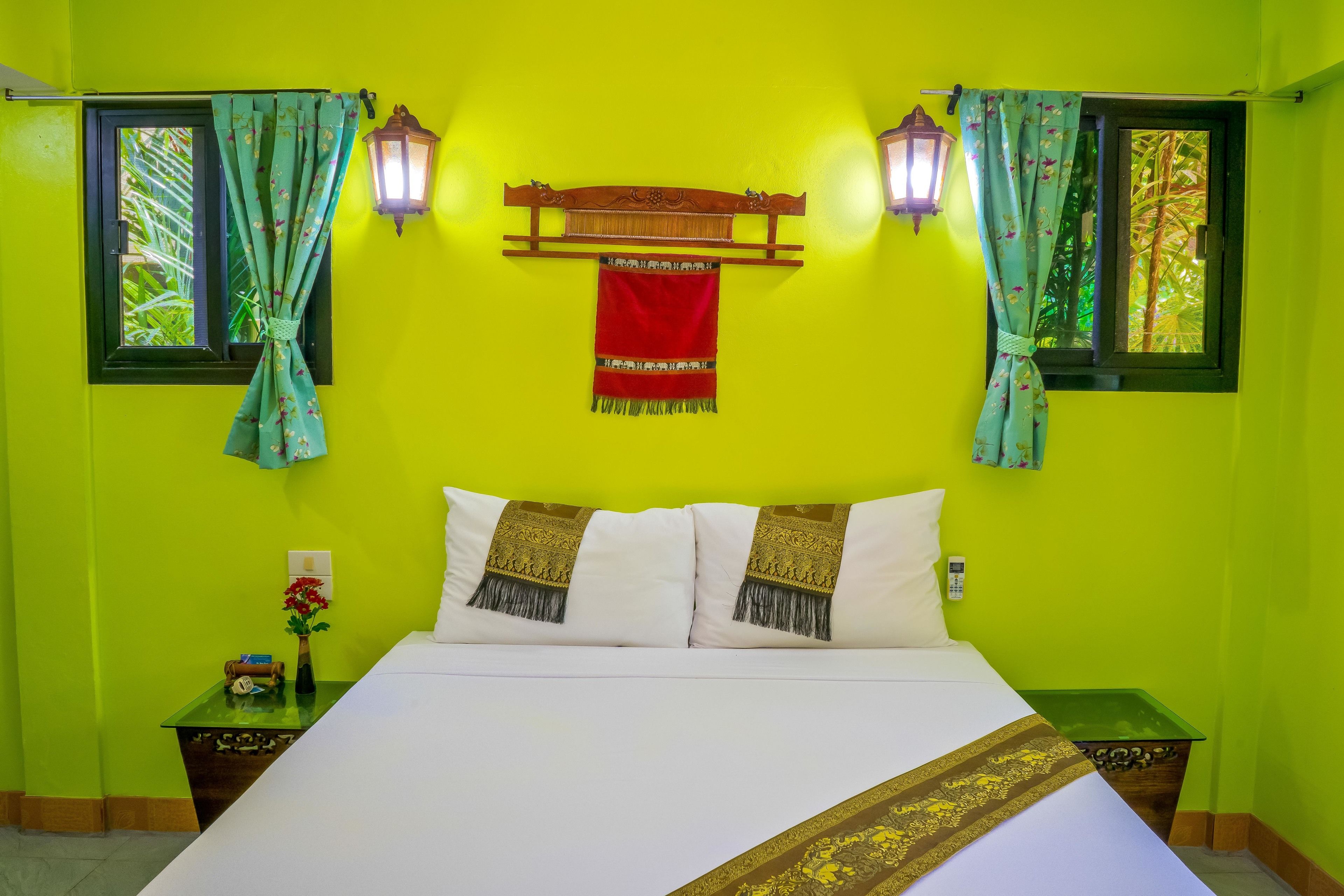 A room with a bed, two nightstands, a window with curtains, a wall-mounted lantern, and a red hanging cloth.