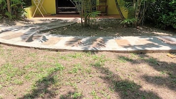 A yellow building with a small garden area, a concrete pathway, and a wooden chair.