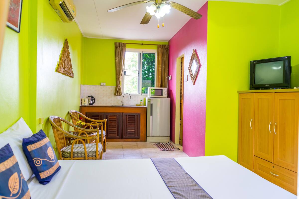Una habitación con cama, televisión, kitchenette y ventilador de techo.