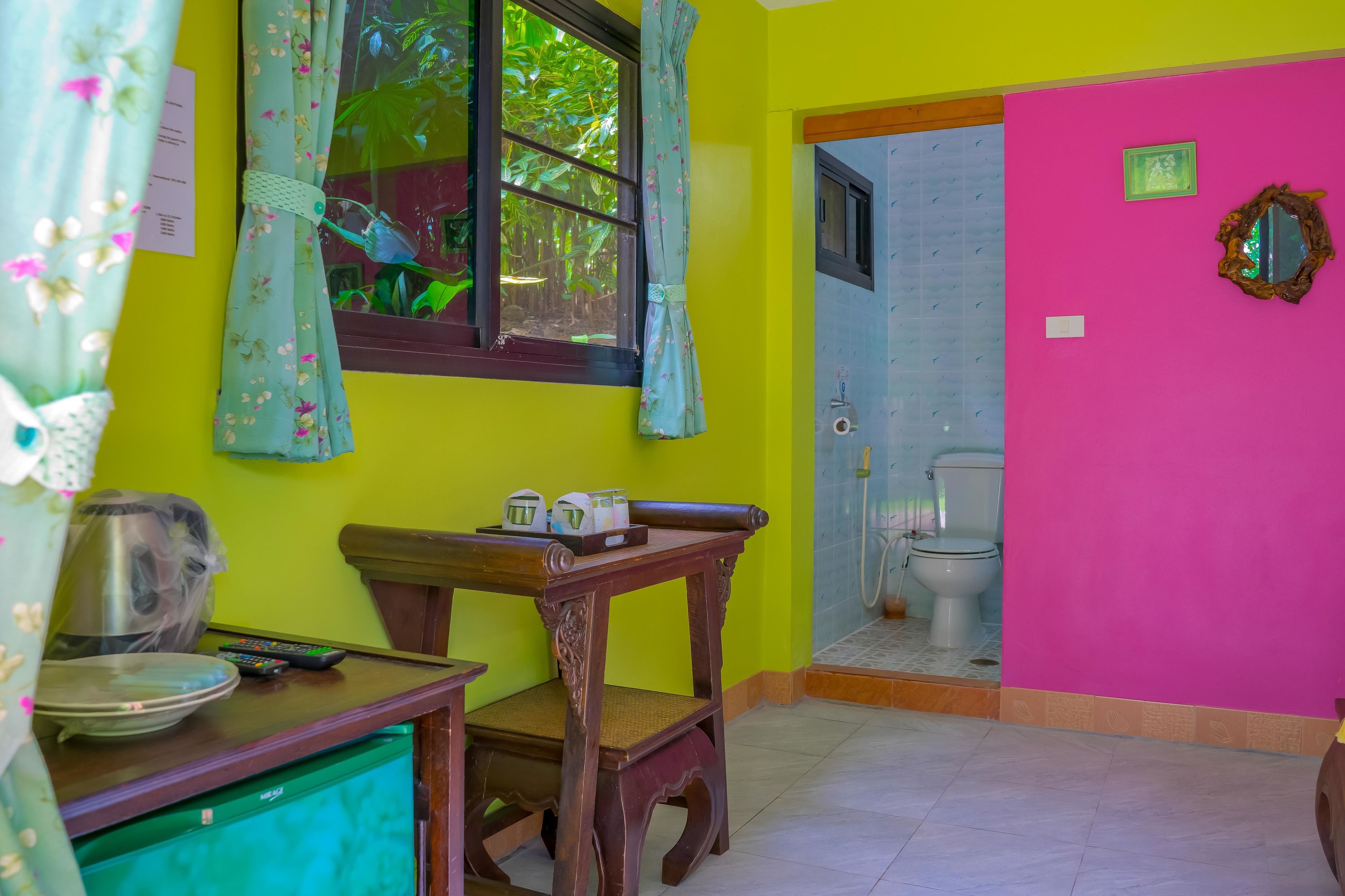 A room with a wooden table, a green cabinet, a window with floral curtains, and a pink wall.