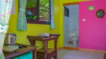 A room with a wooden table, a green cabinet, a window with floral curtains, and a pink wall.