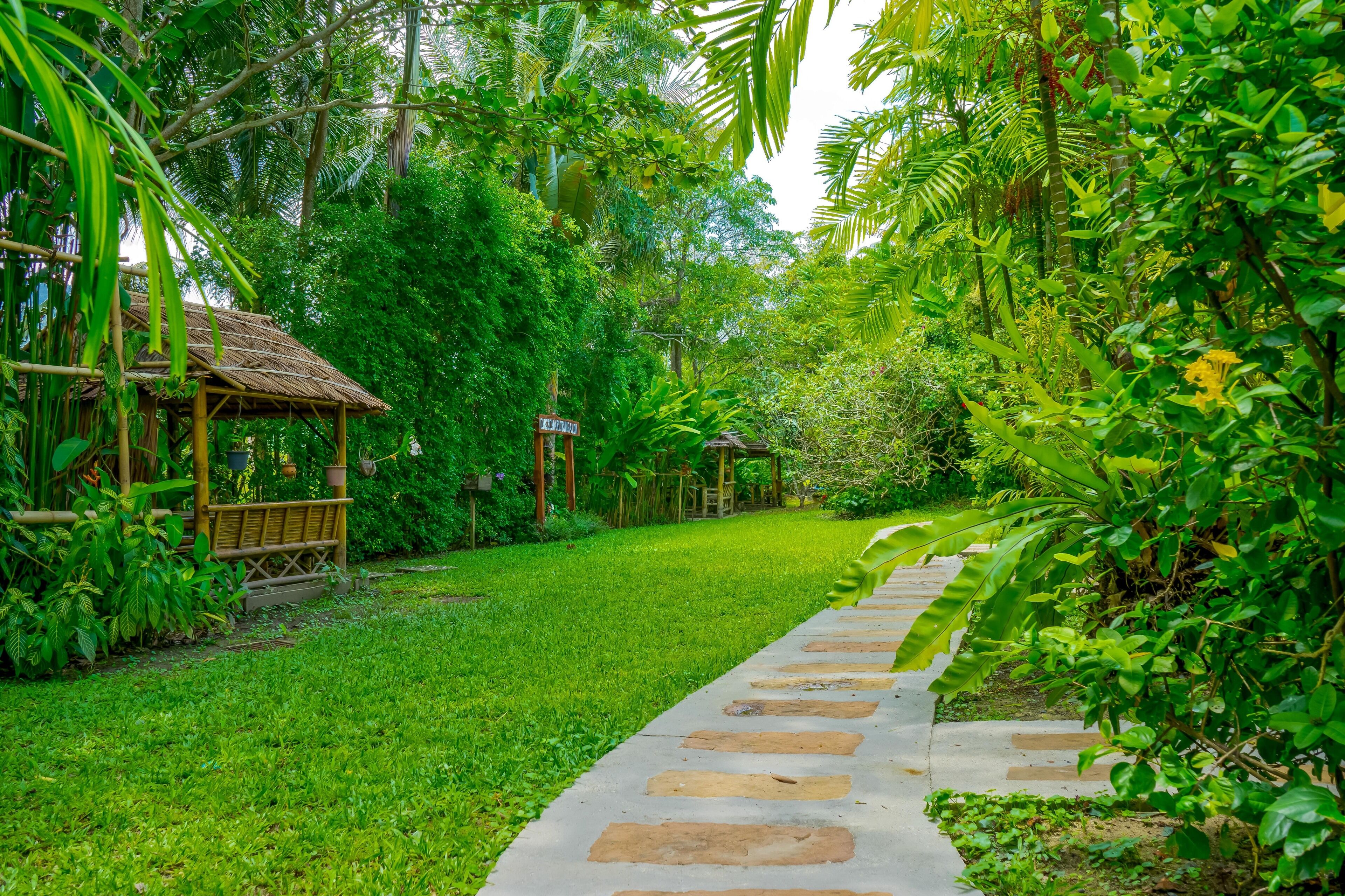 A pathway leading through a lush garden with a bamboo structure on the left.