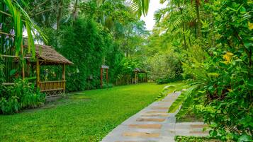 A pathway leading through a lush garden with a bamboo structure on the left.