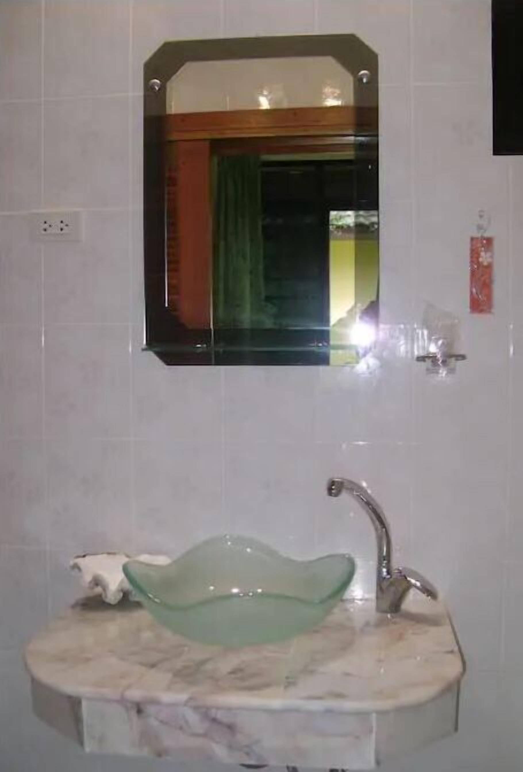 Une salle de bain avec un lavabo en marbre, un bol en verre vert, un miroir et un distributeur de serviettes.