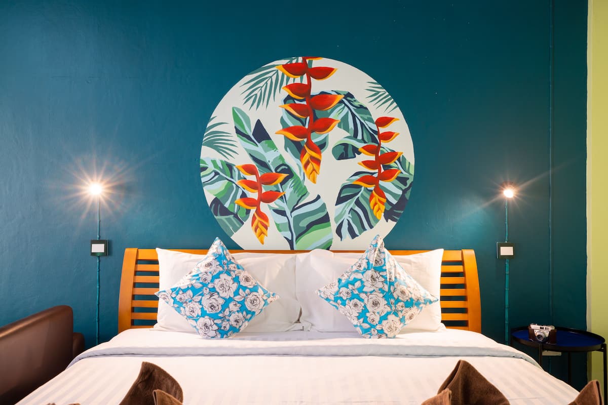 A hotel room with a bed, two pillows, a nightstand, and a wall painting.