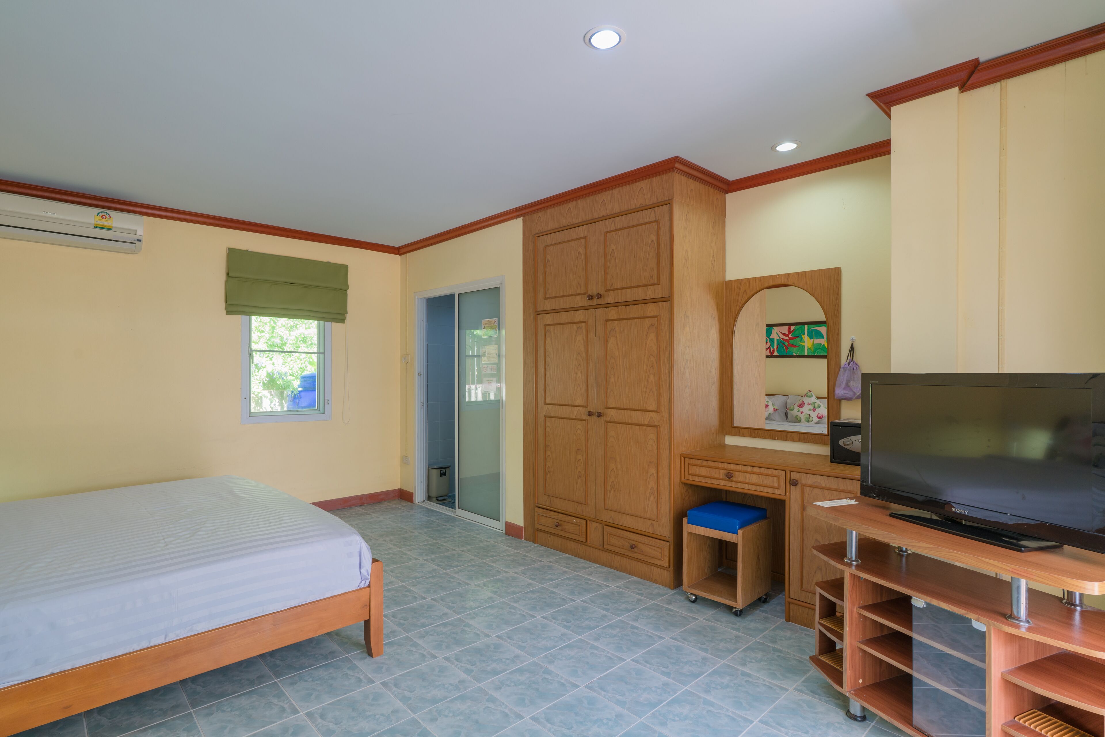 A bedroom with a bed, a TV on a wooden stand, a wardrobe, and a sliding door closet.
