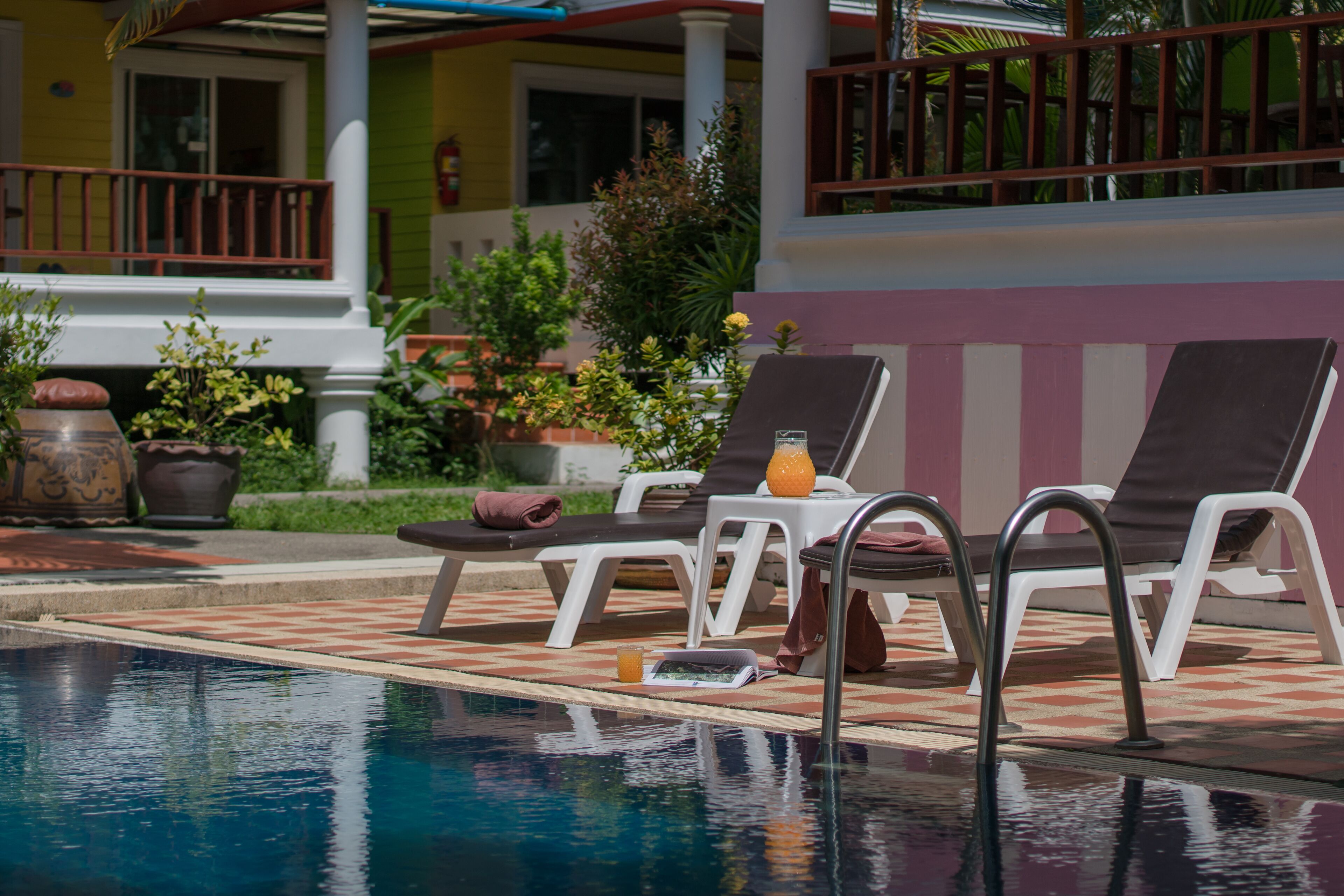 A pool area with lounge chairs, a table with a drink, and potted plants.