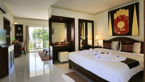 A hotel room with a large bed, a desk with a computer, a TV, a large mirror, and a balcony with a view of trees. - Naka Resort (Kamala)