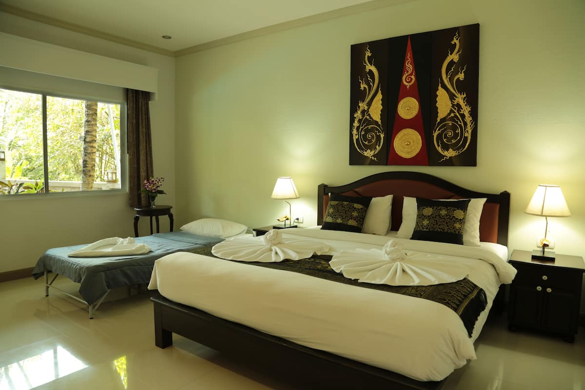 A hotel room with a large bed, a smaller bed, two bedside tables with lamps, a window with curtains, and a wall with a decorative painting.