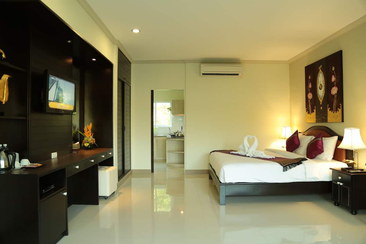 A modern hotel room with a large bed, bedside tables, a desk, and a view into the kitchen.
