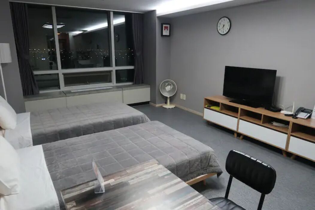 A hotel room with two beds, a TV, a desk, and a window with a city view.