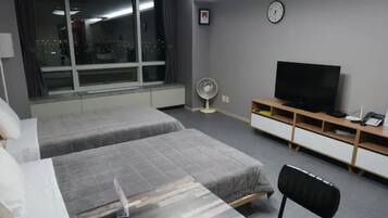 A hotel room with two beds, a TV, a desk, and a window with a city view.