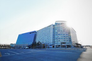 Un hotel moderno con fachada de vidrio, diseño de esquina curva y un estacionamiento frente a él.