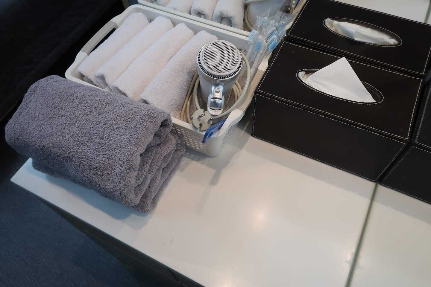 Un baño con un perchero que sostiene toallas dobladas, un secador de pelo y una caja de pañuelos negros.