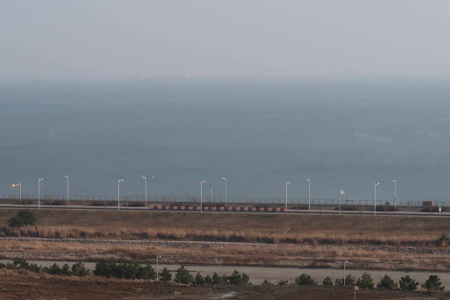 A coastal landscape with a road, streetlights, and a distant view of the sea.
