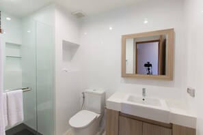A modern bathroom with a glass shower enclosure, a white toilet, and a wooden vanity with a sink. - Sugar Palm Residence (Phuket)