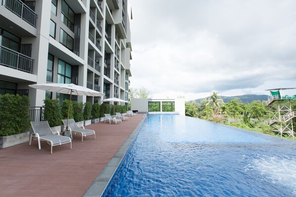 A swimming pool with lounge chairs and umbrellas, surrounded by a modern building with balconies. - Sugar Palm Residence (Phuket)