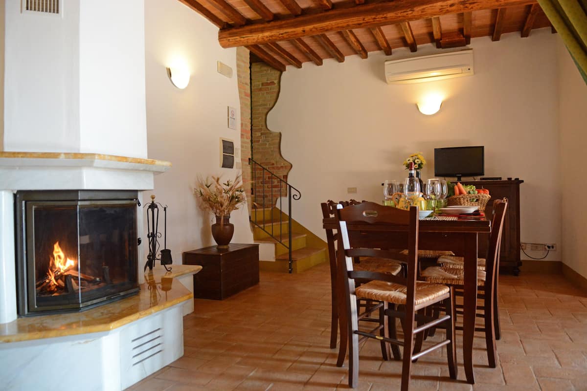 A living room with a fireplace, wooden dining table, chairs, and a staircase.