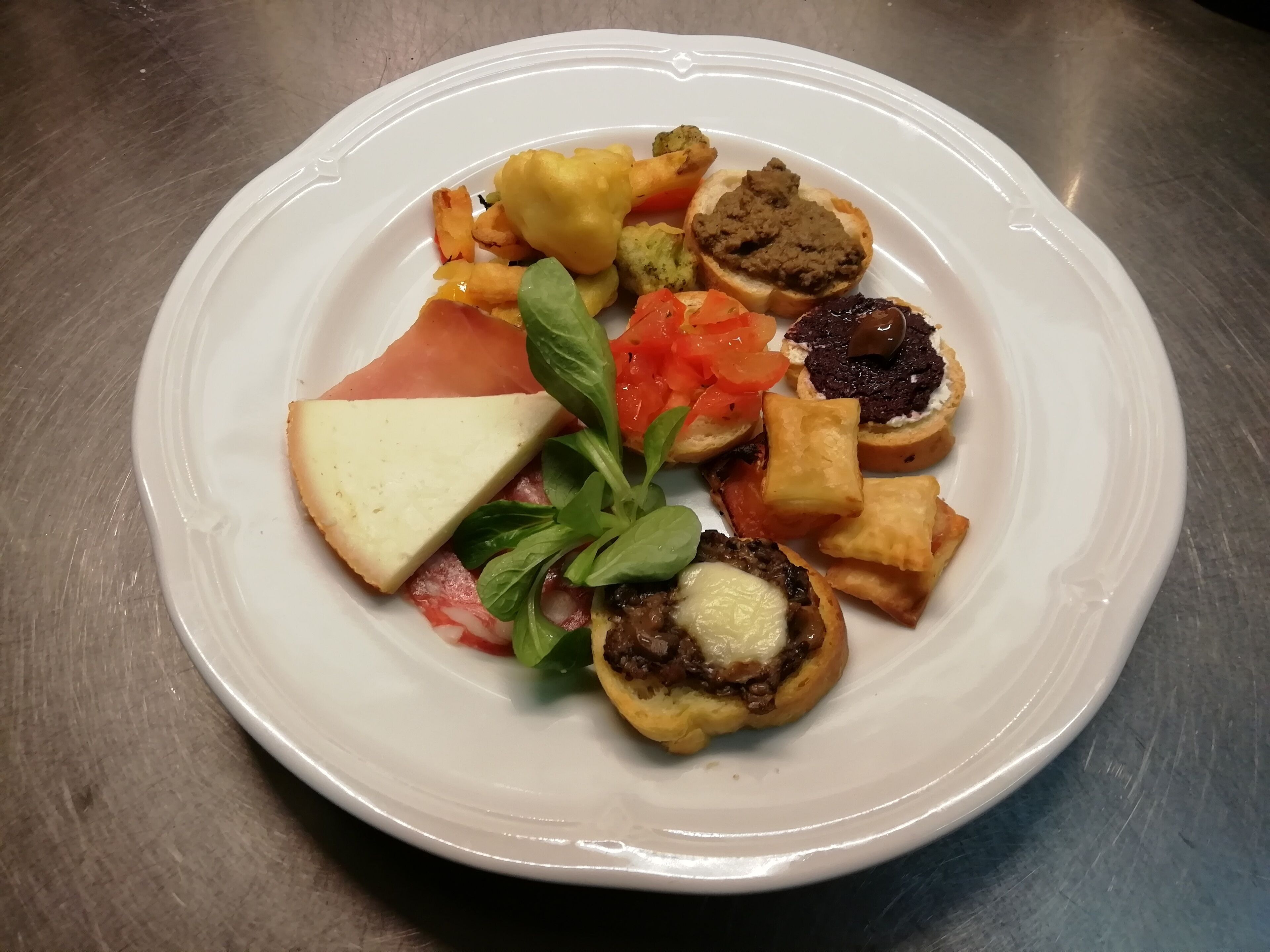 Une assiette blanche contenant divers aliments, notamment une tranche de fromage, un morceau de viande et plusieurs petites pâtisseries.