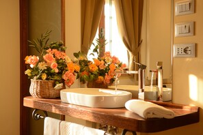 Une salle de bain avec un lavabo, un miroir et une serviette. Il y a deux paniers de fleurs sur le comptoir.